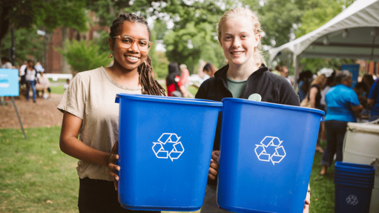 Two students, each holding a blue recycle bin